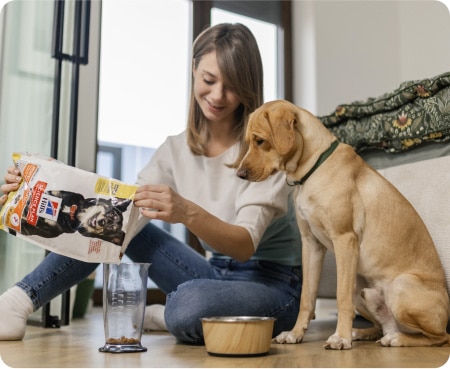 Bir köpek dikkatle bakarken bir ölçü kabına Hill's Pet Nutrition maması döken bir kadın.