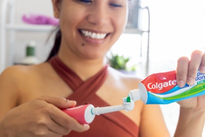 Banyoda diş fırçasına Colgate diş macunu sürerken gülümseyen bir kadın.